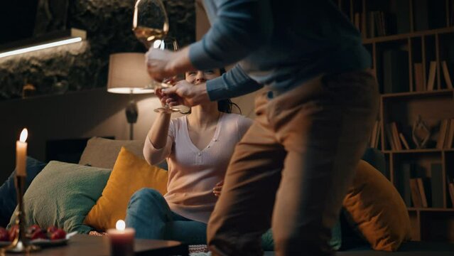 Romantic husband bringing wine to smiling wife sitting couch. Couple having date