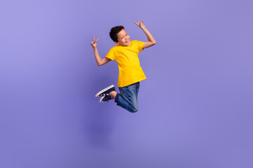 Fototapeta na wymiar Full length photo of nice young pupil boy jumping showing double v-sign wear yellow garment isolated on purple color background