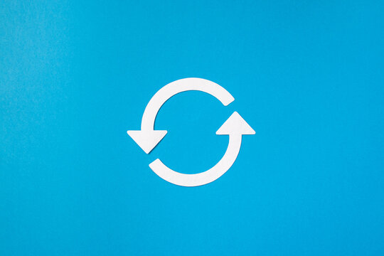 Recycling symbol cut out of white paper on blue background, top view. Concept of ecology and paper recycling. Recycled. Eco arrow reuse material.