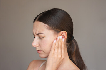profile of a young brunette woman suffering from otitis. She frowns, closes her eyes, presses her...