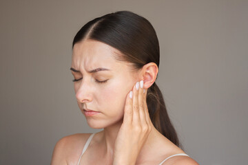 Caucasian brunette woman is experiencing acute pain in her ear. She frowns, closes her eyes,...