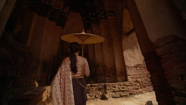 Young beautiful Asian woman wearing thai traditional dress holding umbrella in hand walking at ancient temple with old pagoda in Wat Chai Wattanaram Ayutthaya, Thailand
