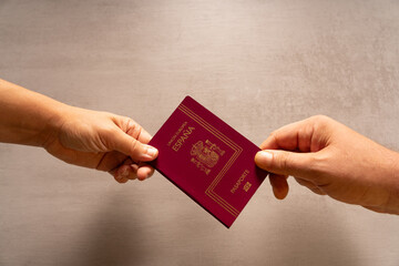 A hand of a man and another of a woman hold a passport. On a table in the background