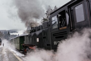 Naklejka premium Vintage steam locomotive chugging down a set of railroad tracks, emitting plumes of smoke