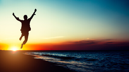 Silhouette young woman jumping with hands up on the beach at the sunset. Travel photo summertime - obrazy, fototapety, plakaty