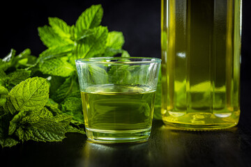 Sweet mint syrup and mint leaves on black table.