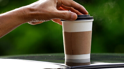 coffee takeaway in a paper cup on top of the car roof green tree background at sunrise in the morning,  selective focus, soft focus.