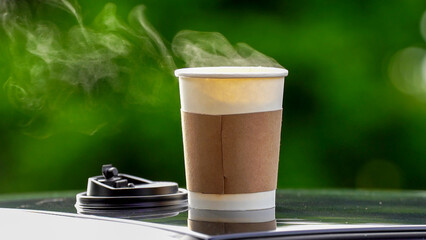 coffee takeaway in a paper cup on top of the car roof green tree background at sunrise in the morning,  selective focus, soft focus.