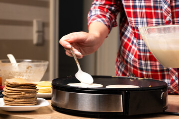 Woman cooking delicious crepe on electric pancake maker in kitchen, closeup - obrazy, fototapety, plakaty