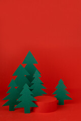 Christmas tradition background - red scene, cylinder podium mockup for presentation gifts, cosmetic products surrounded green paper spruce forest, vertical. New year template for card, poster, flyer.