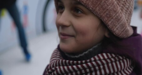 Extreme close-up hand of mother taking care of a Caucasian girl in warm scarf and jacket in winter, straightening her pink knitted hat at the skating rink. It's frosty outside,happy child is smiling - Powered by Adobe