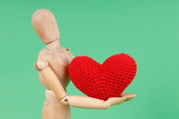 A wooden mannequin holds a red knitted heart. This image can be used to represent love, affection,...