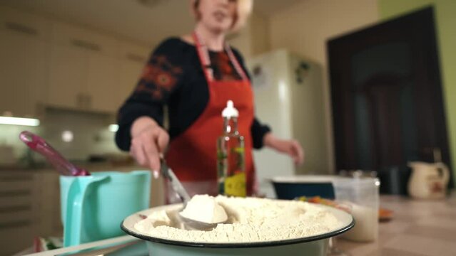 The hostess in the kitchen prepares the dough mixture. Women's hands pour a spoonful of flour into a bowl and stir the mixture. Preparation of Passover for Easter. Baking pasak cupcakes and bakery