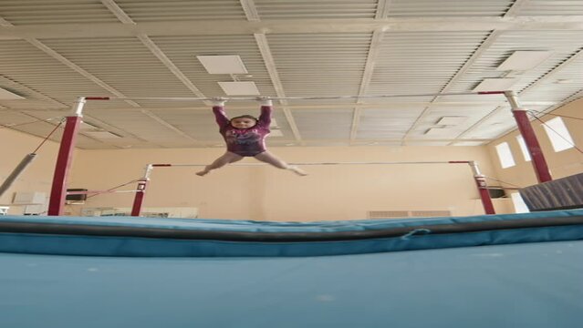 Low angle vertical stab shot of determined Biracial little girl doing double handstand split on gymnastics bar and landing straightly on mat while rehearsing for performance in studio