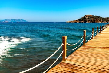 Obraz premium breeze on the sea. wooden pier with safety ropes and wavy seascape by sunny day