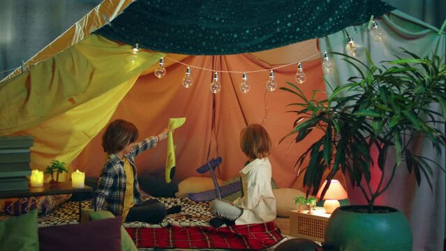 Two young boys are messing around with toy airplanes inside a big blanket tent which has very bright lighting and is decorated in a very modern way to create a comfortable atmosphere
