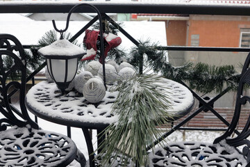 Pine branch and Christmas baubles in the snow. First snow fell on metal garden furniture. Christmas mood.