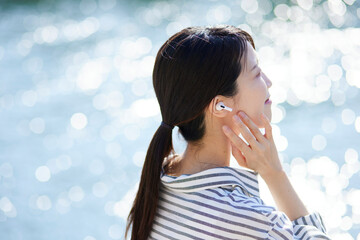 川辺でワイヤレスイヤホンで音楽を聴く日本人の女性