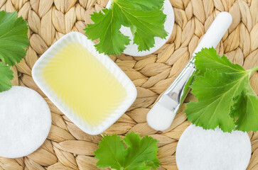 Small white bowl with cosmetic (massage, cleansing) aroma oil and geranium leaves. Natural skin...