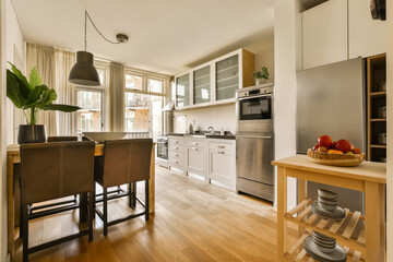 a kitchen and dining area in a small apartment with wood floors, white cabinets, stainless appliances and an island table