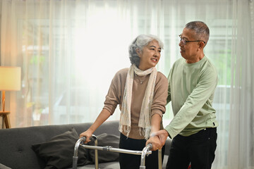 Fototapeta na wymiar Smiling senior man helping his wife walking with walker at home. Elderly healthcare concept