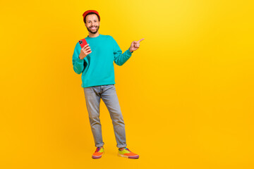 Fototapeta premium Full size photo of handsome guy wear teal sweatshirt hold smartphone indicating at offer empty space isolated on yellow color background