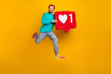 Fototapeta na wymiar Full size photo of optimistic guy wear jeans red beanie hat flying run with big red heart in hands isolated on yellow color background
