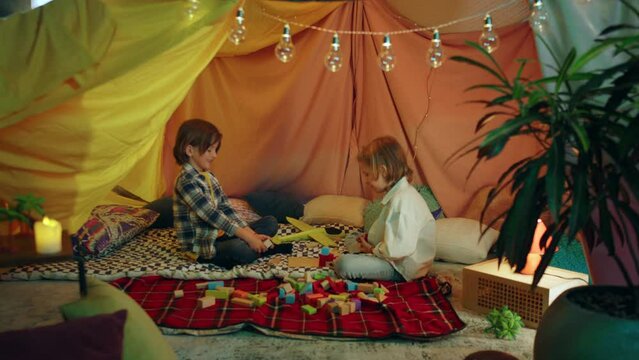 A zooming out shot of two young boys playing together in a handmade sheet tent indoors enjoying one another s company
