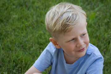 Portrait of a blond boy looking to the side against the backdrop of a green lawn copy space