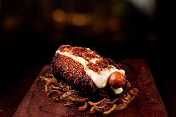 American hot dog with black bread and crispy onion on wooden board