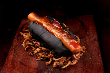 Typical Halloween witch's finger hot dog on black bread with ketchup blood served on wooden board...