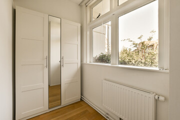 a room with white walls and wood flooring, there is a large window looking out to the garden outside