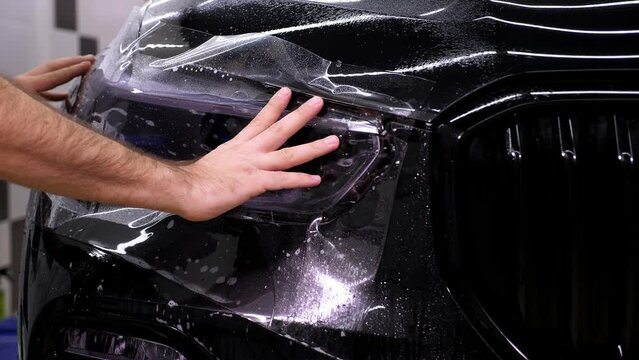 Car wrapping specialist putting vinyl foil or film. Protective film on the vehicle. Applying a protective film to the car with tools for work. Car detailing. Transparent film. Car paint protection.