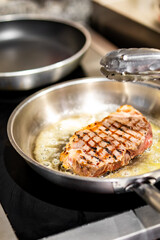 Professional chef cooking beef steak in frying pan on stove in restaurant kitchen