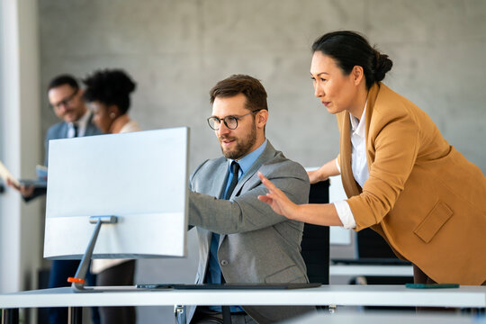 Senior business manager talking with experienced colleague while using computer in office.