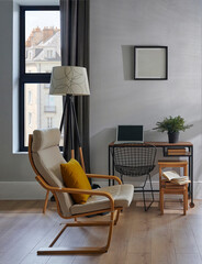 Decorative room chair, table, laptop, vase of plant, lamp and frame in front of the grey wall, brown curtain, parquet interior design, working corner.