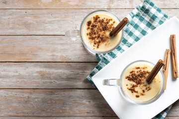 Homemade eggnog with cinnamon on wooden table. Typical Christmas dessert. Top view. Copy space