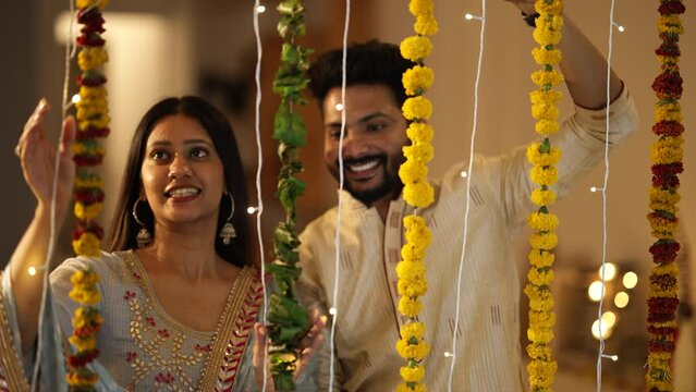 An Indian man and his beautiful wife decorating their house with marigold flowers and lights - an Indian festival. A married couple dressed in ethnic wear for the festival of Diwali.