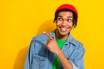 Photo of dreamy charming man wear jeans shirt red hat looking pointing finger empty space isolated yellow color background
