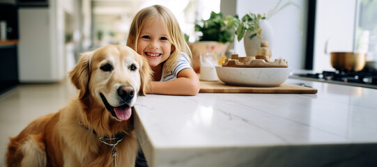 Beautiful little girl is posing with a golden retriever dog at the kitchen table. Cute baby and her pet preparing for breakfast at home. Happy smiling girl and puppy enjoy their time spent together.