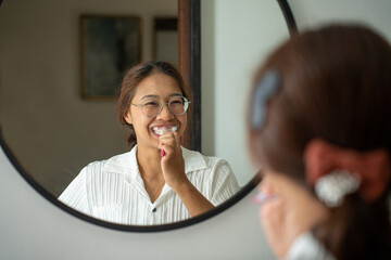 morning brushing teeth. Young woman brushing teeth with toothbrush and looking in mirror in bathroom. Oral hygiene, healthy teeth and care.