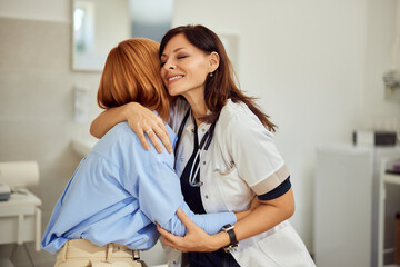 A brunette doctor hugging a female patient, just finished an appointment. - obrazy, fototapety, plakaty