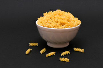 Uncooked Fusilli Pasta in White Bowl on Black Table. Raw and Dry Macaroni. Unhealthy and Fat Food. Italian Culture