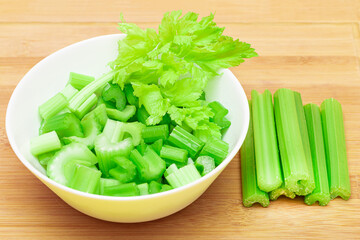 Fresh Chopped Celery Slices in White Bowl with Celery Sticks on Bamboo Cutting Board. Vegan and Vegetarian Culture. Raw Food. Healthy Diet with Negative Calorie Content