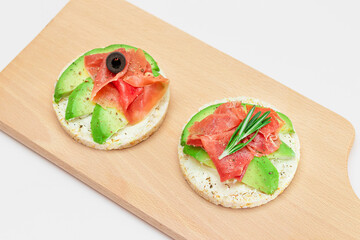 Rice Cake Sandwich with Avocado, Jamon, Olives and Rosemary on Wooden Cutting Board. Easy Breakfast. Quick and Healthy Sandwiches. Crispbread with Tasty Filling. Healthy Dietary Snack
