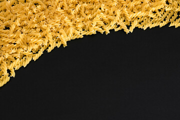 Uncooked Fusilli Pasta with Copy Space on Black Background. Raw and Dry Macaroni. Fat and Unhealthy...