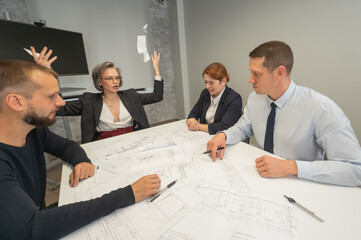 Four business people sitting around a table discussing blueprints. Designers engineers at a meeting. 