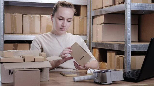 Female warehouse worker online store owner using laptop at work preparing parcel boxes checking ecommerce shipping online retail e commerce store order fulfillment in dropship delivery post office