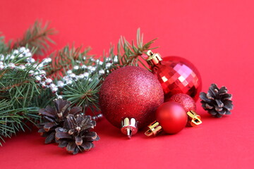  Red Christmas balls of different sizes with spruce branches lie on a red background.