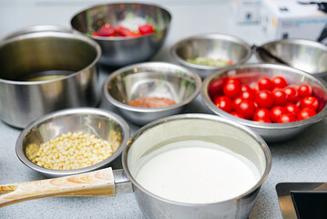 set of stainless steel bowls and pans with raw products, pine nuts, cherry tomatoes, heavy cream in a gravy boat